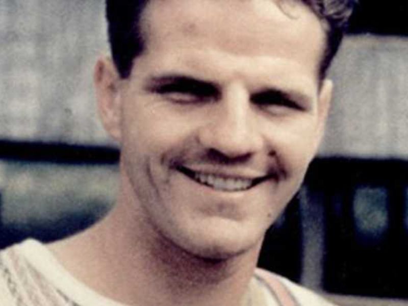A smiling man with light brown hair and a strong jawline, wearing a casual shirt, in front of a blurred background.